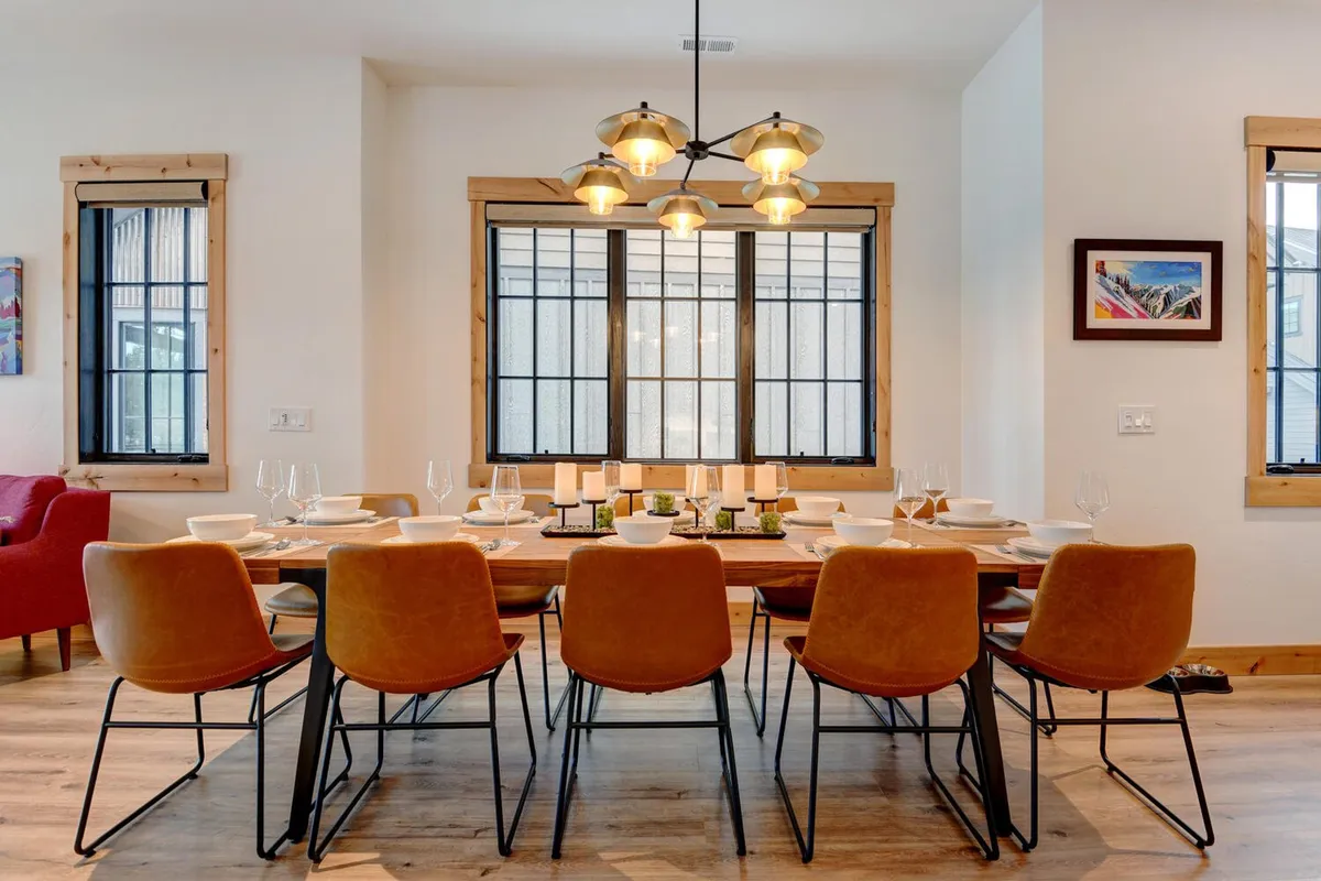 A spacious dining area with a large, custom wood table that seats 10, illuminated by a chic chandelier. Windows bring in plentiful natural light, and the decor is both refined and welcoming, ideal for celebrations or casual meals.