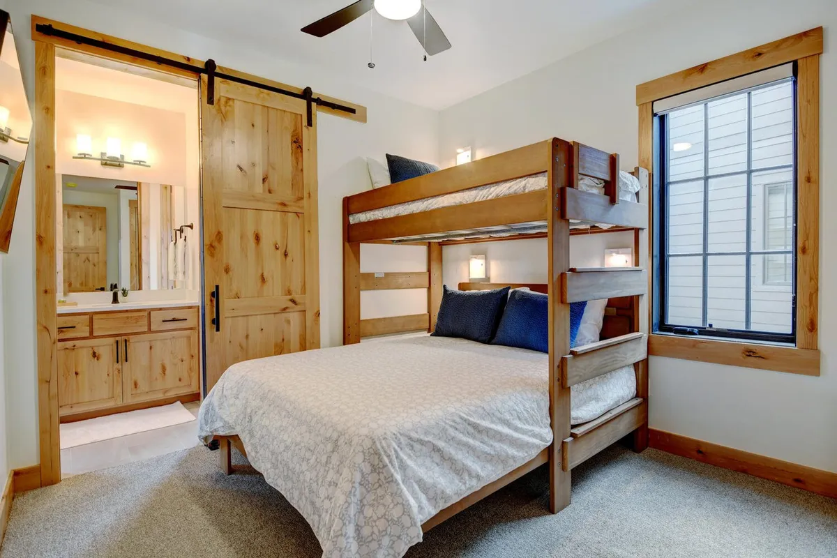 A welcoming bunk bed area with a large window, wall-mounted lights, and simple, modern decor. Natural light flows in, making the space inviting for children or teens to relax, read, or share stories before bed.