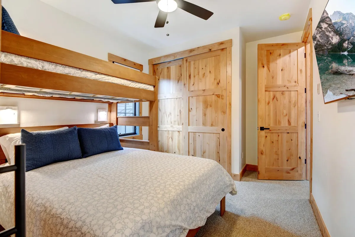 A welcoming bunk room featuring a twin-over-queen bunk bed and a separate queen bed, with cozy wooden doors and a restful layout. The space is designed for families and kids, emphasizing flexibility and comfort.