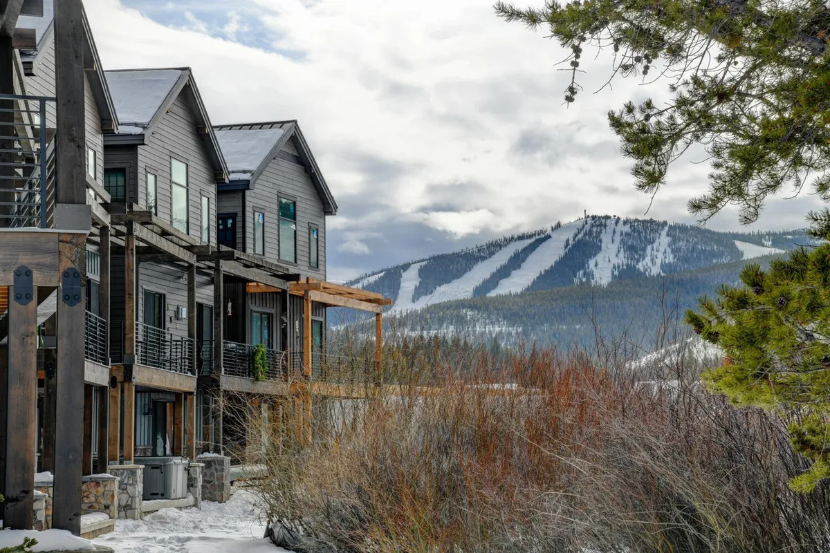A dramatic view of mountain slopes with modern wooden balconies in the foreground. The architecture suggests luxurious alpine living, while the scene captures the adventurous outdoor lifestyle available just steps from the property. The image hints at both relaxation and activity, including skiing and hiking.