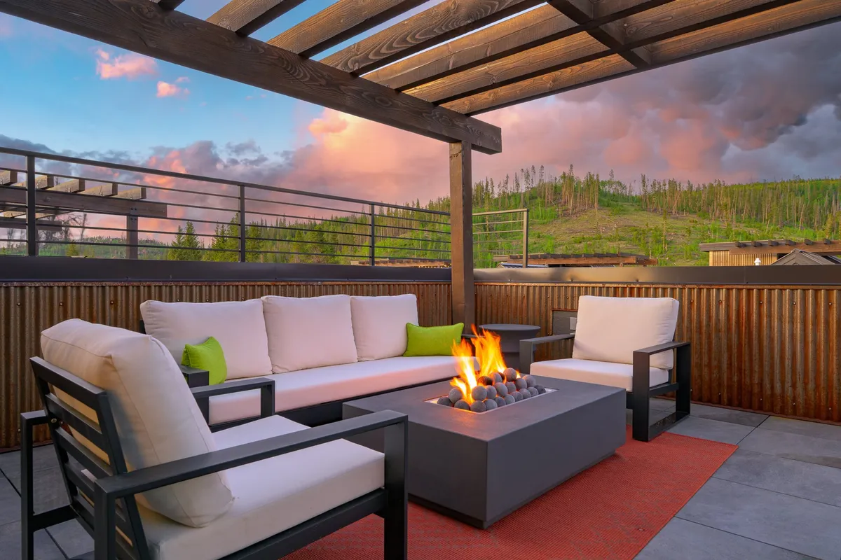 This exterior image shows a cozy fire pit area with comfortable couch seating set against a scenic landscape backdrop. The space is open and inviting, perfect for relaxing outdoors after a day of adventure. The setting exudes tranquility and encourages both human and pet guests to unwind together in the fresh mountain air.