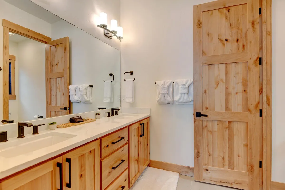 A modern bathroom with a double sink vanity, expansive mirror, wooden door, and neatly arranged towels. The space feels both luxurious and relaxing, reminiscent of a spa retreat.