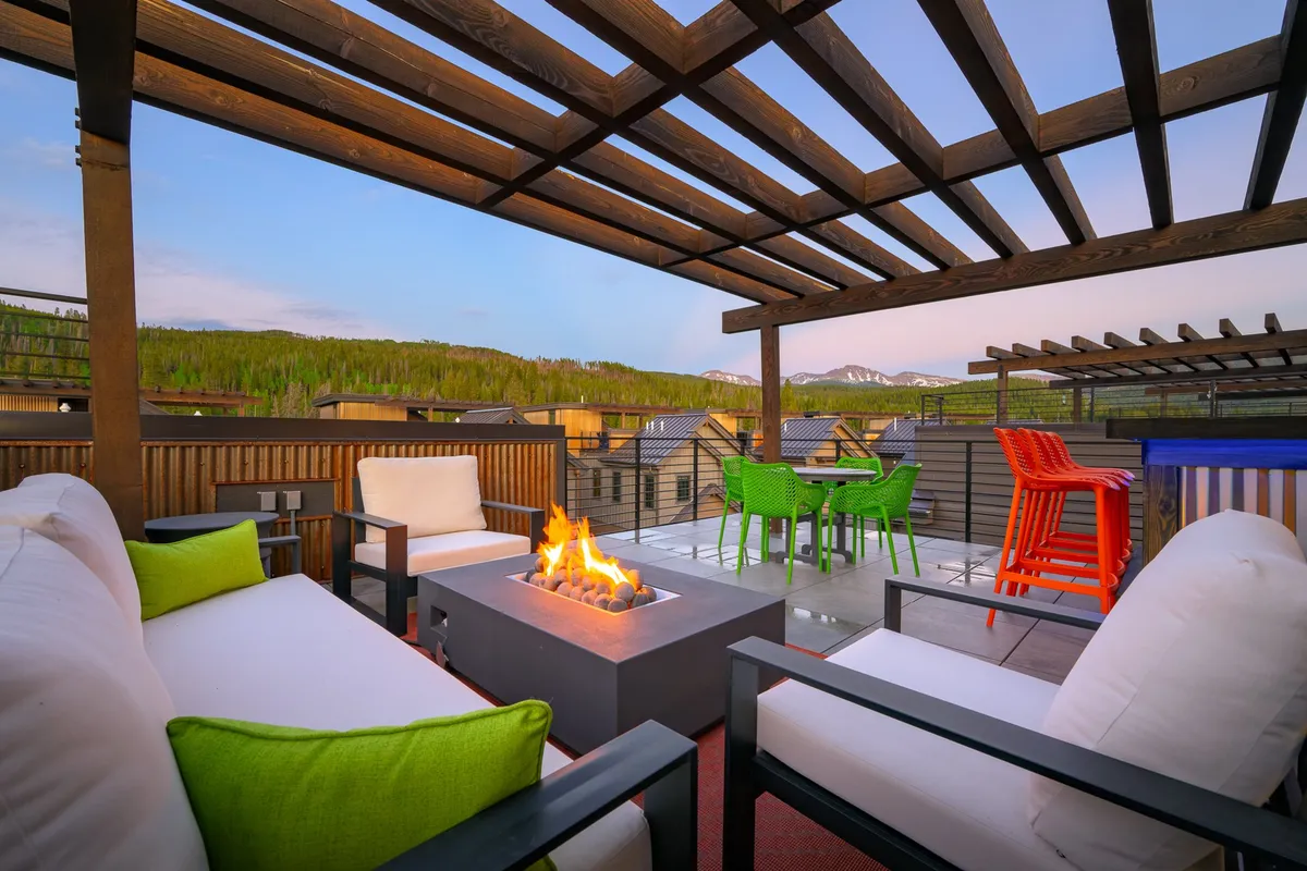 An inviting outdoor seating area with a fire pit surrounded by colorful chairs, offering a clear view of the mountains in the distance. The environment is vibrant and communal, ideal for social gatherings or quiet relaxation with pets.